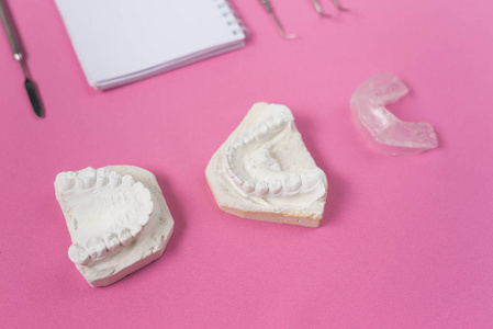 在粉红色的背景是一个牙科仪器和石膏铸造的牙齿