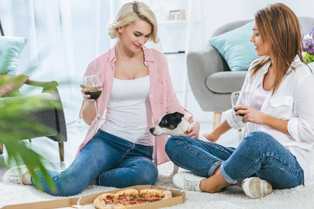 女孩和狗坐在地板上，拿着比萨饼和一杯红酒