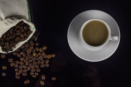 在黑暗的背景下，在茶托上放一小杯适当的咖啡，再配上从袋子里倒出来的咖啡豆