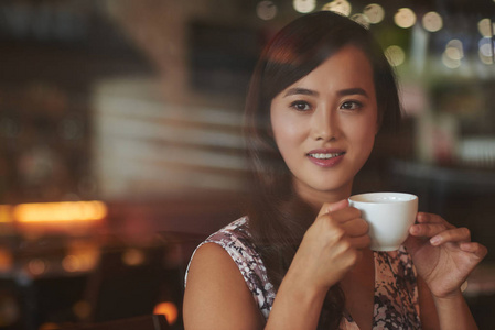 有魅力的中国女孩，端着一杯咖啡坐在