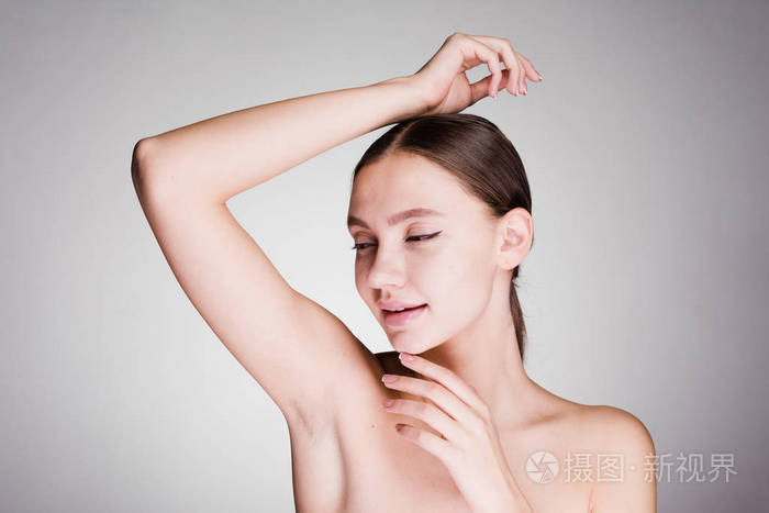 在一个灰色的背景下, 一个女人淋浴后看着腋窝的皮肤