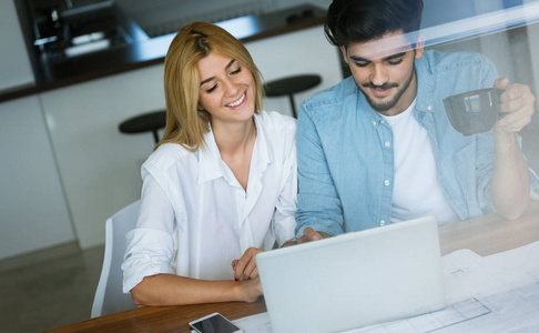 一对充满爱意的年轻夫妇使用笔记本电脑并用文件分析他们的财务状况的照片
