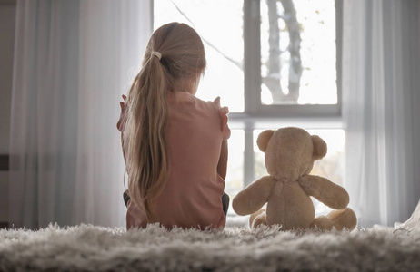 小女孩与泰迪熊坐在地板上的房间。自闭症概念