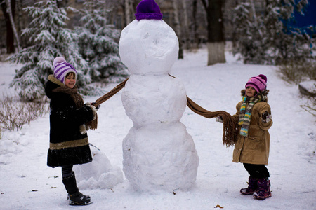 一个快乐的小女孩为一个大雪人戴上围巾。可爱的小妹妹在冬天的公园里玩得很开心