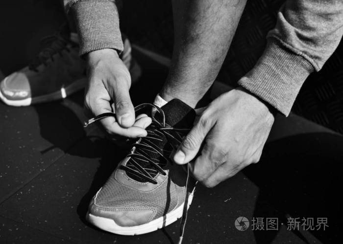 在健身馆,男人在运动鞋上系鞋带,黑白的