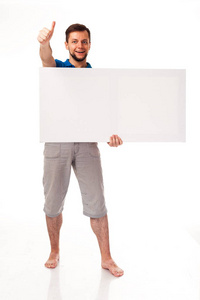 一个留着胡须摆着白色标志的人。 可用于放置广告标识等。 穿着蓝色T恤和灰色裤子。