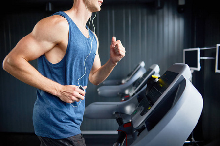 戴着耳机在跑步机上跑步在现代健身房进行强化锻炼时欣赏最喜欢的歌曲的肌肉男