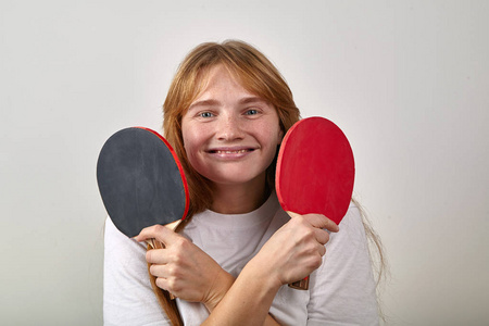 戴着白色t恤交叉双手拿着乒乓球拍的红发雀斑微笑女人的画像