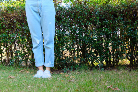 希普斯特休闲白色运动鞋。穿着白色鞋子和蓝色牛仔裤的女性站在草地上，自然背景非常适合任何用途