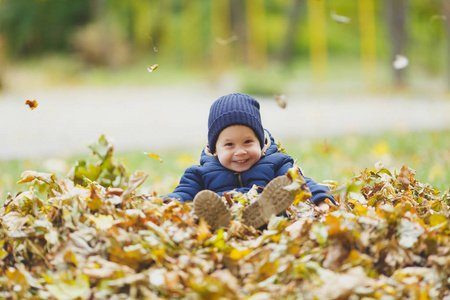 小可爱的孩子在秋天公园里走着, 坐在一堆树叶上, 扔着干枯的黄色秋叶。小男孩休息。亲子, 家庭日 5月15日, 爱, 父母, 孩