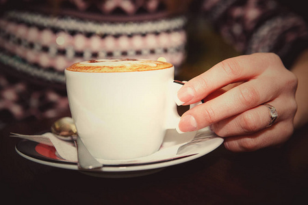 女人的手在木桌上端着一杯咖啡