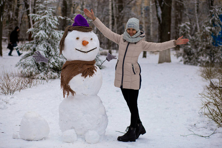 时髦的女人雕刻一个真正的雪人。冬天，美丽的女人在冬天的公园里玩得很开心