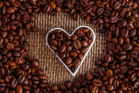 用咖啡豆制成的心形咖啡框架在Burlap纹理上。咖啡豆的形状在心脏的背景上被解雇。 情人节快乐