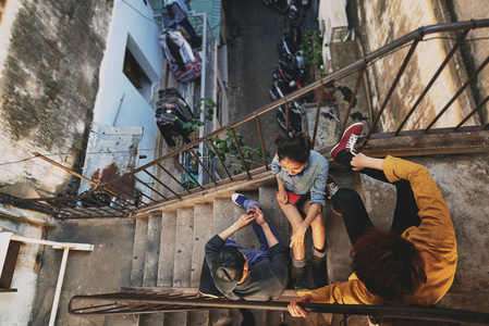 时尚的亚洲青少年在城市贫民窟闲逛的高角度视角他们坐在破旧公寓的楼梯上，互相交谈