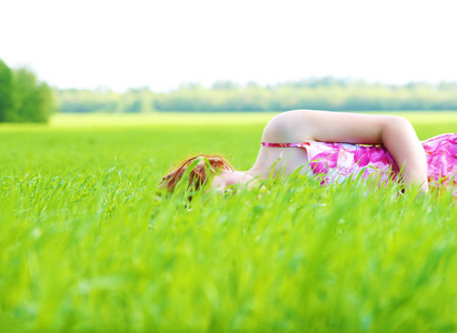 穿着红色夏装的年轻女孩躺在新鲜的绿草中，在温暖的土地上放松。