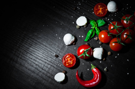 食物背景。 红色辣椒，樱桃，番茄，罗勒，黑胡椒，马扎雷拉球，盐，深色木制背景，复制空间。 顶部视图
