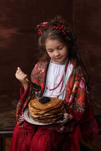 穿着俄罗斯服装的女孩把煎饼和黑色鱼子酱放在一起