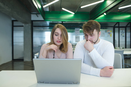 一个男人和一个女孩坐在一个现代化的办公室在桌子上, 看着一台笔记本电脑。工作中的项目讨论。办公理念