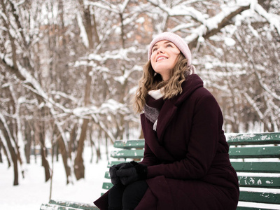 在一个下雪的冬天公园里, 快乐漂亮的年轻女子站在长凳旁