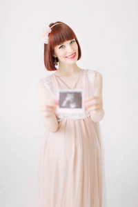 年轻孕妇手持超声胶片站在白色背景下