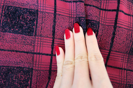 美容红色指甲用凝胶抛光。 女人的手与红色指甲上的红色苏格兰织物背景伟大的任何用途。