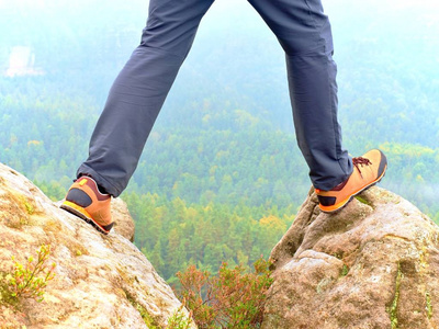 双腿徒步旅行者在舒适徒步靴在岩石上。在室外的浅色裤子，皮鞋的男人腿
