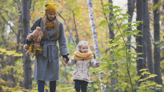 与她的母亲和泰迪熊秋天公园散步的小女儿