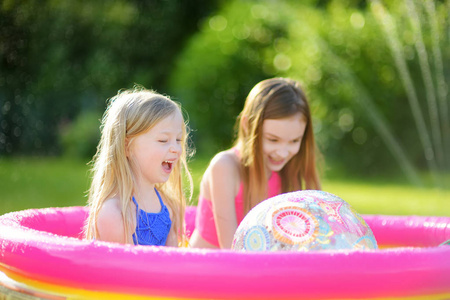 可爱的小女孩在充气婴儿池里玩。 快乐的孩子在炎热的夏天在五颜六色的花园游戏中心飞溅。 孩子们的暑期活动。
