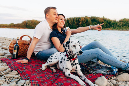 幸福的年轻夫妇与狗在 roadtrip 的肖像。男人和女人坐在格子上户外野餐概念