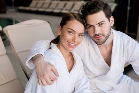 漂亮的年轻夫妇穿着浴袍，在水疗中心的摄像机前拥抱和微笑。