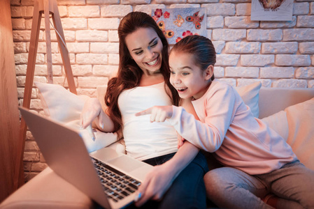 妈妈和小女儿晚上在家里用笔记本电脑看电影。