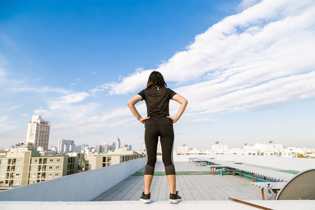 运动跑步的妇女穿着黑色健身服站在蓝天建筑的顶部