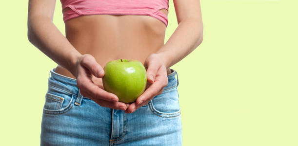 饮食观念。美丽的女人与苗条的腰部是抱着苹果在柔和的背景