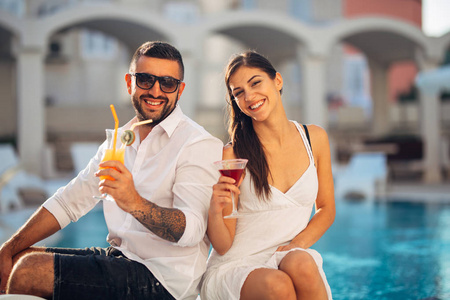 吸引人的一对夫妇在异国度假胜地的游泳池附近享受暑假。参加夏日泳池朗日酒吧派对，沙滩派对。喝着清爽的冷饮