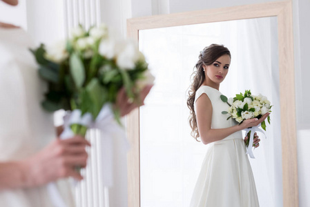 美丽的新娘穿着婚纱，带着结婚花束，看着镜子里的倒影