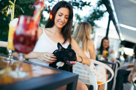 漂亮的年轻女人和她可爱的法国斗牛犬小狗坐在咖啡馆里。 以狗为主题的人