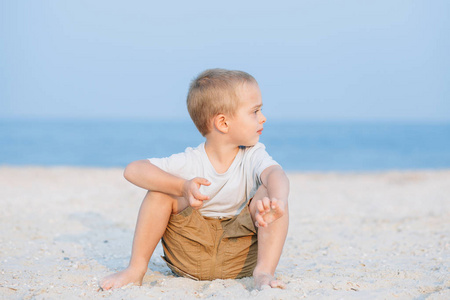 炎热的夏天，一个严肃可爱的小男孩在海滩上水边。 假期玩得开心