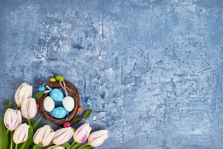 复活节花环白色郁金香和装饰复活节彩蛋的蓝色背景。 顶部视图复制空间