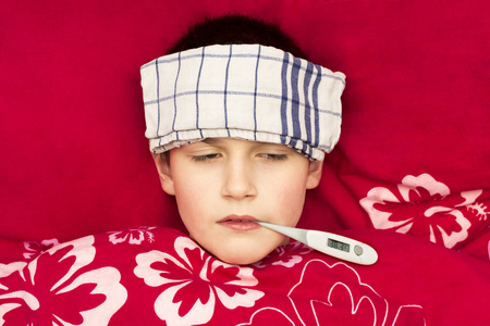 一个生病的男孩躺在床上, 嘴里有温度计。