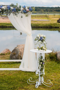 婚礼拱门上装饰着蓝色的花朵和白色的光丝绸。夏季婚礼