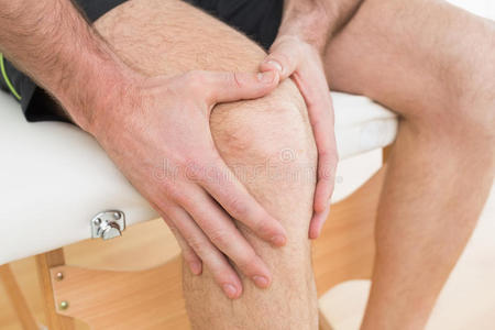 手放在疼痛的膝盖上的人的中段图片