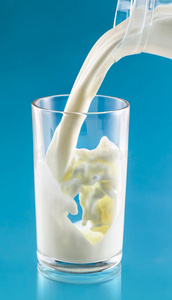 牛奶溅在蓝色背景的透明玻璃上图片
