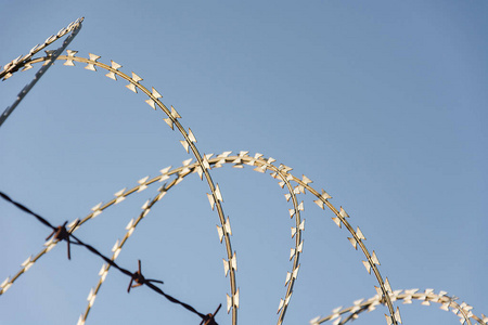 带刺铁丝网用于保护财产和监禁，没有自由，带刺铁丝网在蓝天的栅栏上感到担忧。