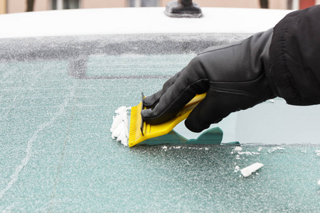 手在手套刮冰从汽车挡风玻璃