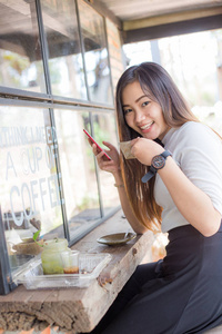商务亚洲女性在现代咖啡店用智能手机发短信，咖啡杯