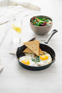 早餐概念白木桌上的煎锅炒鸡蛋，配沙拉和柠檬水