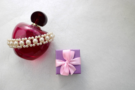 粉红色漂亮的玻璃透明瓶女性香水装饰白色珍贵珍珠和蓝色小礼品盒，并放置一个简单的文字在浅白色背景。
