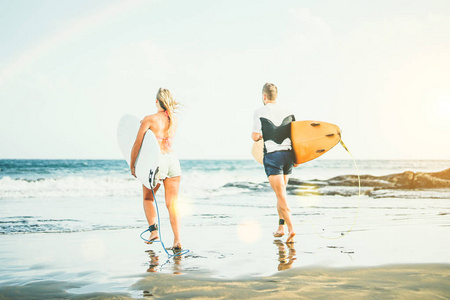 年轻的冲浪者夫妇在日落时带着冲浪板在水中跑步，健康的运动伙伴享受冲浪的一天，人们运动的极端和生活方式