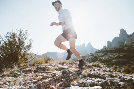 强壮健康的中年人在山公园的生活方式选择上穿着专业的运动服，穿着太阳光耀斑，在超级马拉松或跑步比赛中在岩石和悬崖上奔跑