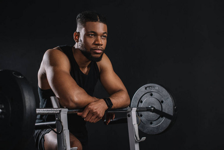 肌肉发达的年轻非裔美国人运动员靠在杠铃上，看着黑人